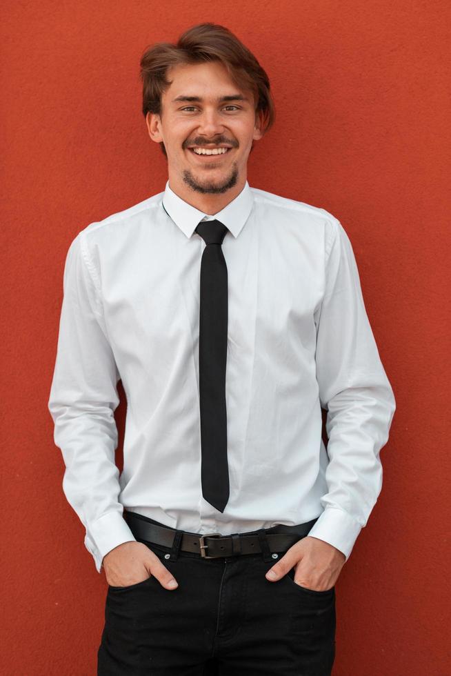 portret van opstarten zakenman in een wit overhemd met een zwart stropdas staand in voorkant van rood muur buiten foto