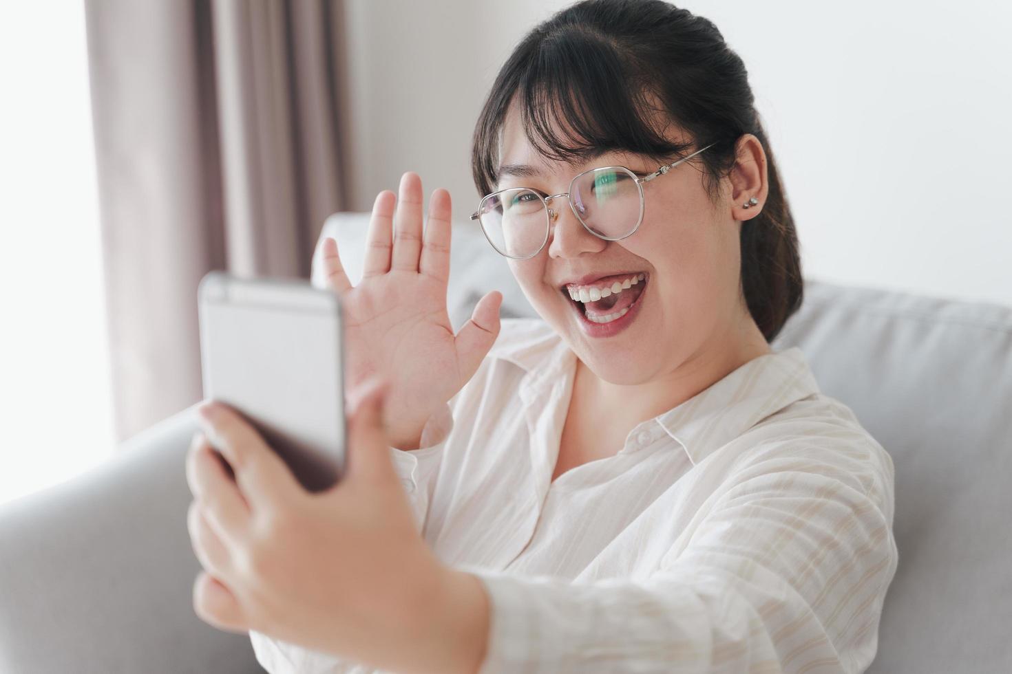 jonge aziatische vrouw die smartphone gebruikt voor online videoconferentiegesprek met vrienden die met de hand zwaaien en hallo gebaar maken foto