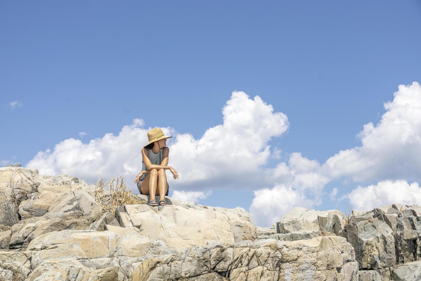 vrouw zittend Aan de rotsen in voorkant van de oceaan met wolken in de lucht foto