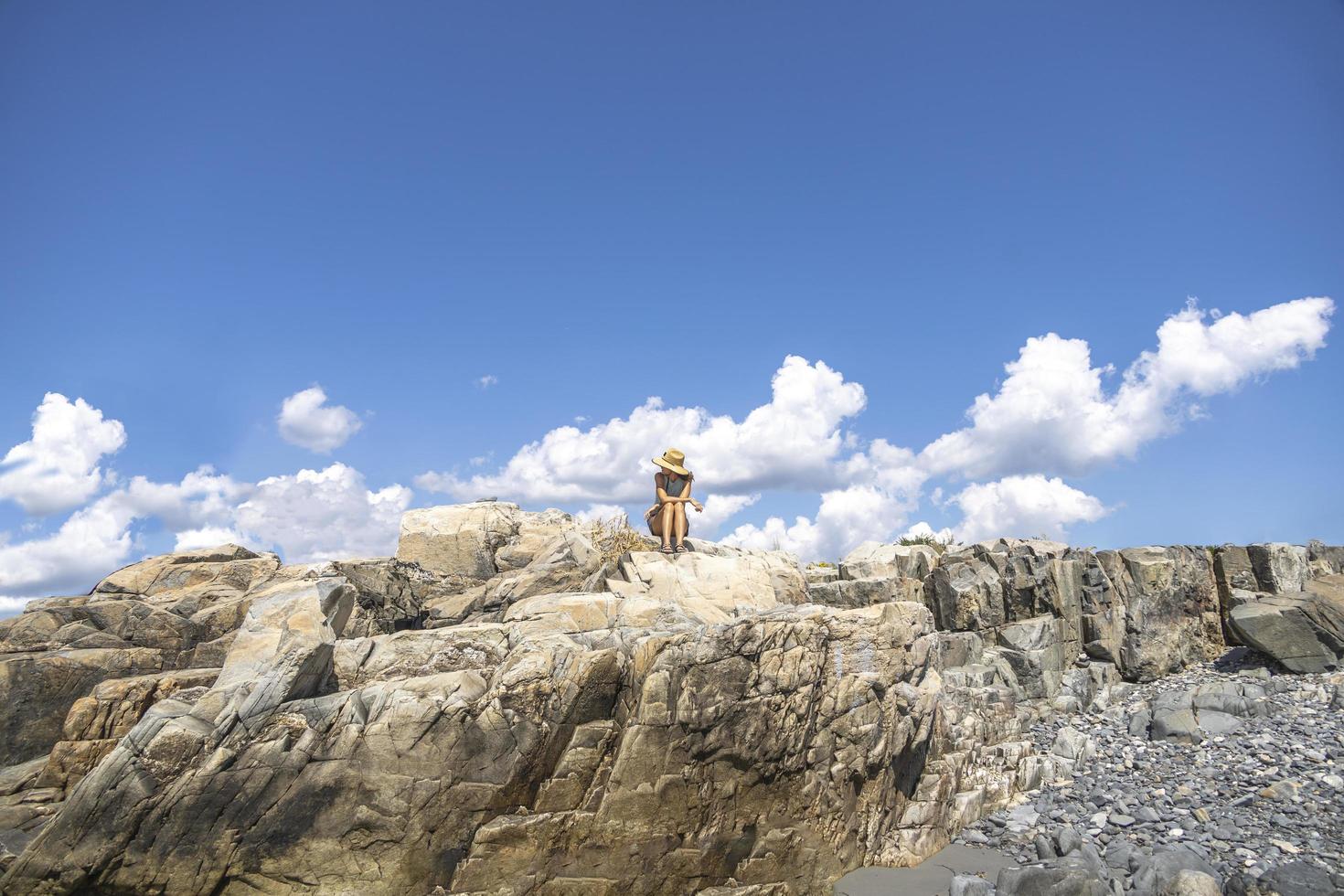 vrouw zittend Aan de rotsen in voorkant van de oceaan met wolken in de lucht foto