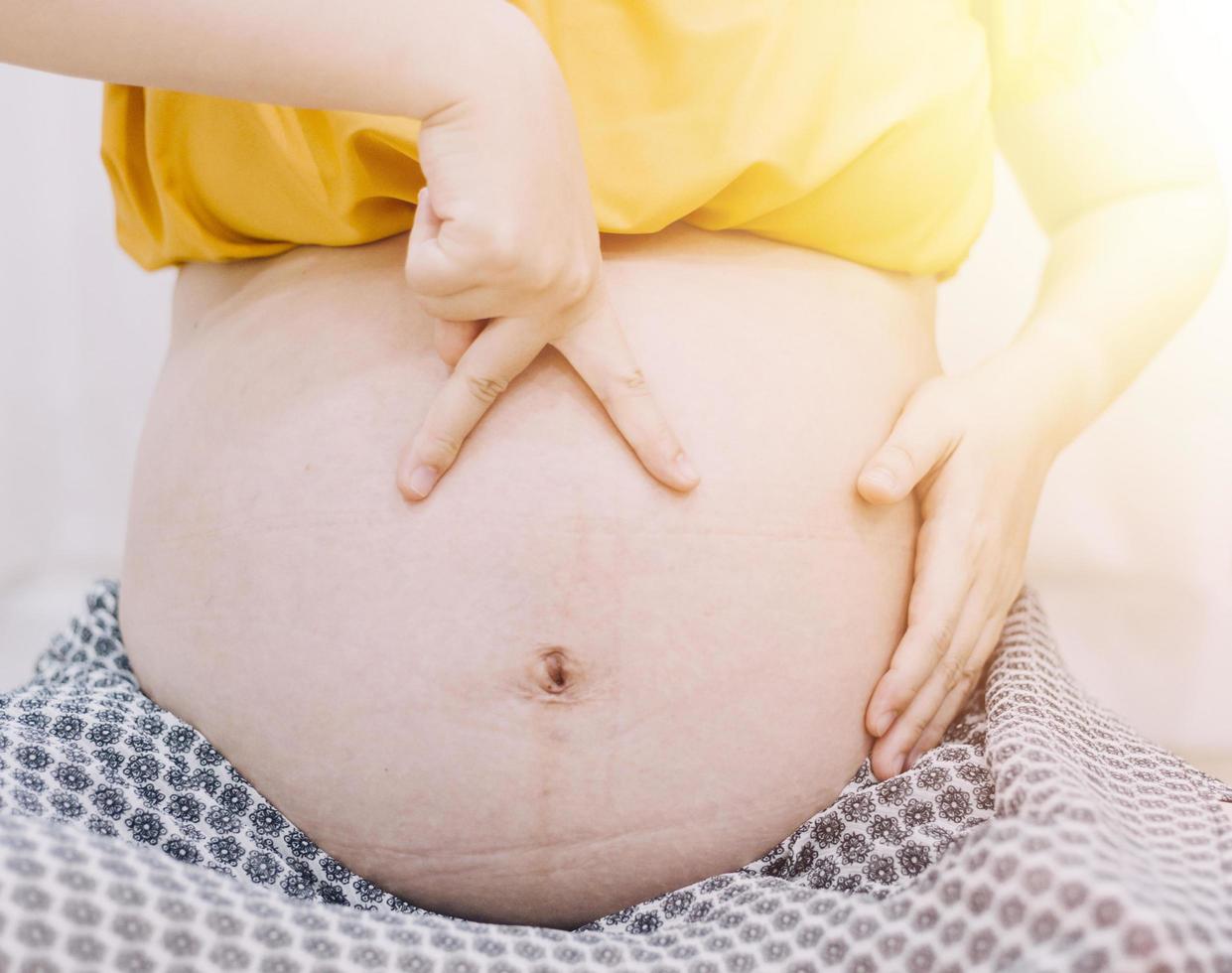 jong volwassen zwanger vrouw in wit kleren aanraken groot naakt buik met handen. tonen vorm geven aan. zwangerschap concept. verwachting tijd. detailopname. geïsoleerd Aan licht grijs muur achtergrond. foto