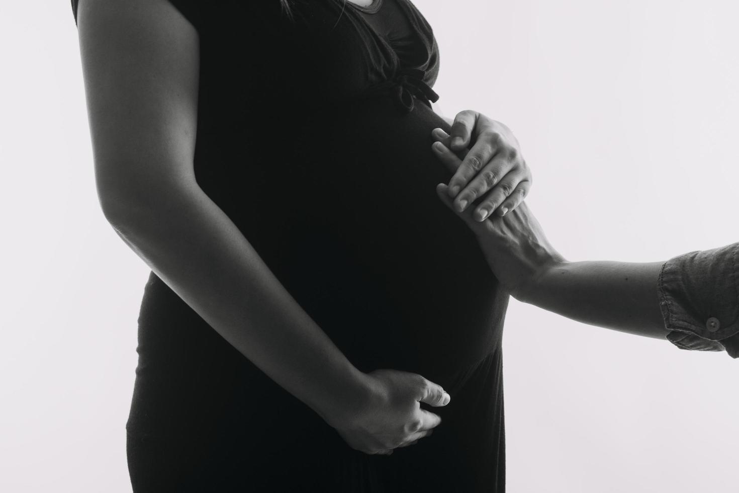 jong volwassen zwanger vrouw in wit kleren aanraken groot naakt buik met handen. tonen vorm geven aan. zwangerschap concept. verwachting tijd. detailopname. geïsoleerd Aan licht grijs muur achtergrond. foto