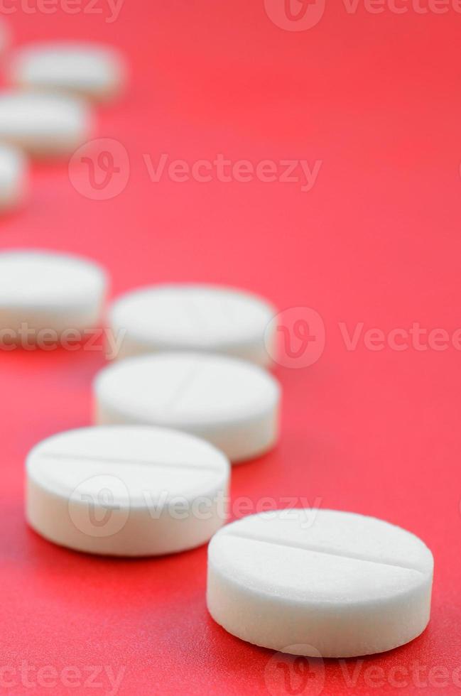 een weinig wit tablets liggen Aan een helder rood achtergrond oppervlak. achtergrond beeld Aan medisch en farmaceutisch topics foto
