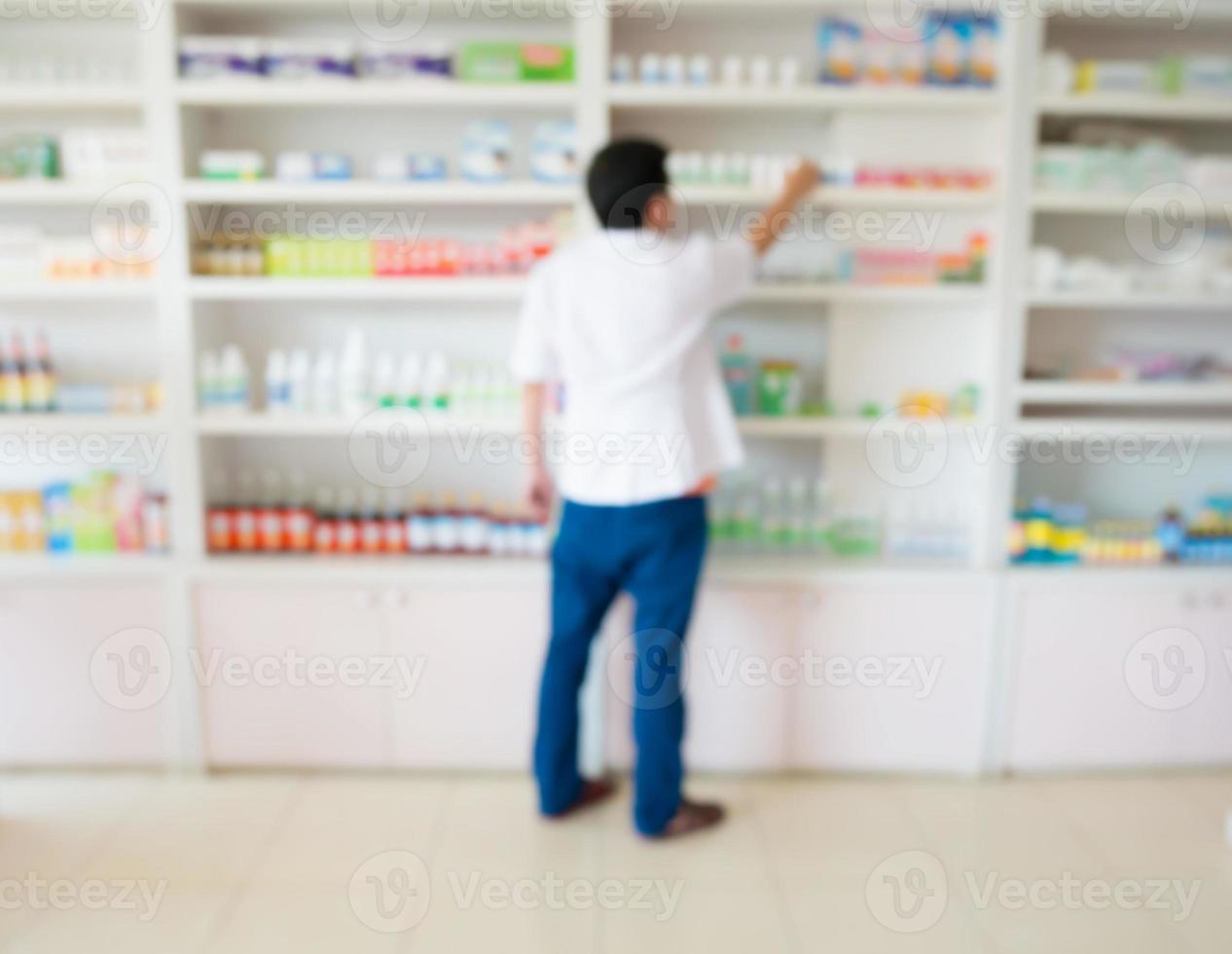 vervagen apotheker die medicijnen van de plank in de apotheek neemt foto