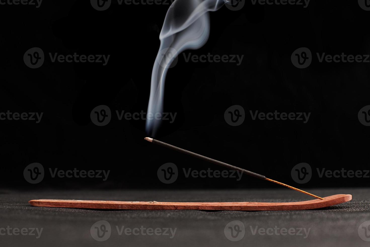 rook krullen van brandende wierookstokjes in houten houder voor ontspanning en meditatie zwarte achtergrond foto