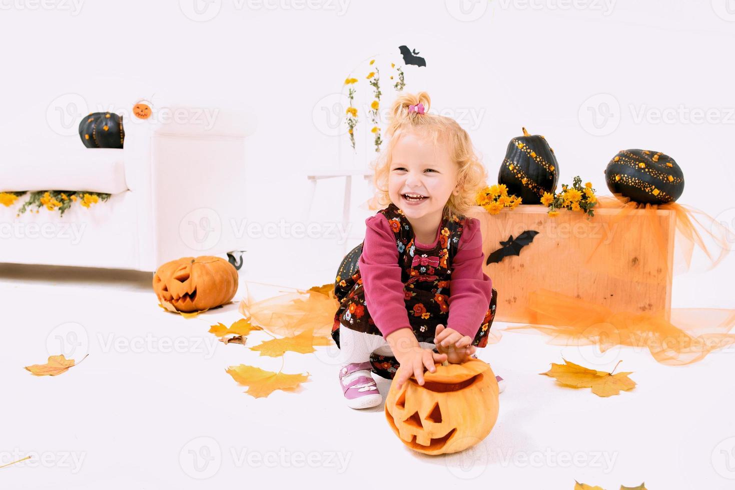 grappig en schattig weinig blond kromme meisje met pompoen in halloween decoratie foto