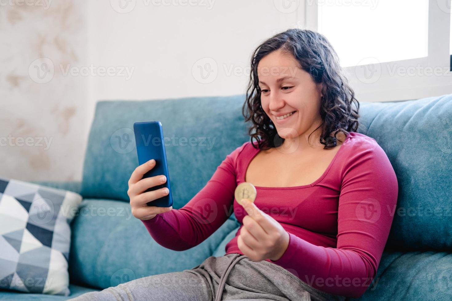 gelukkig vrouw boodschappen doen Aan haar cel telefoon met een bitcoin munt in haar hand- foto