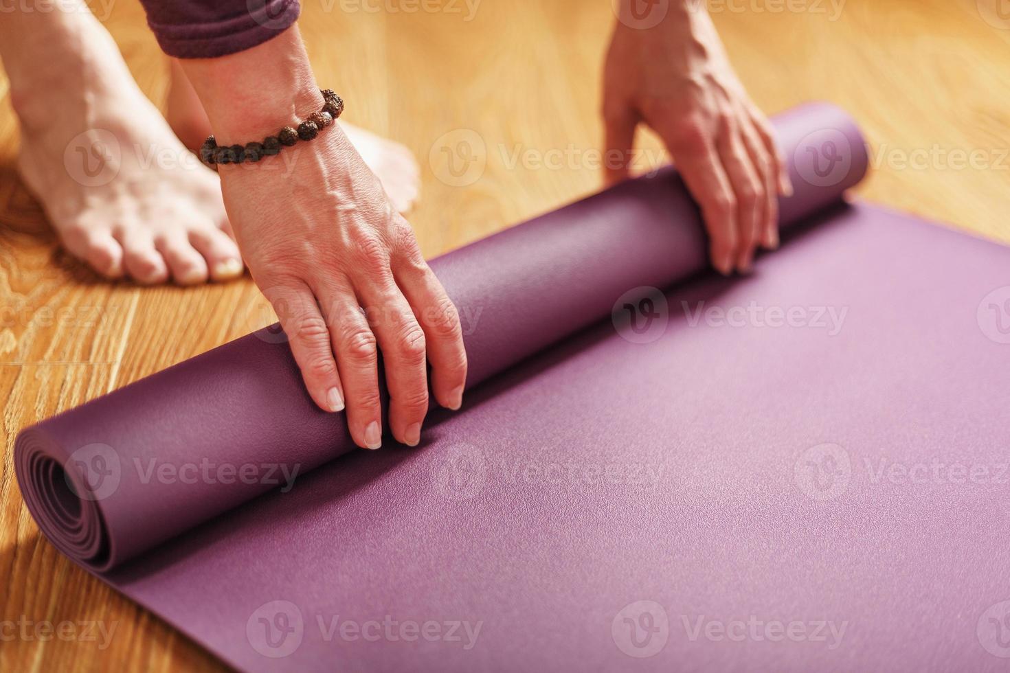 een meisje legt uit een lila yoga mat voordat een training praktijk Bij huis Aan een houten vloer. foto