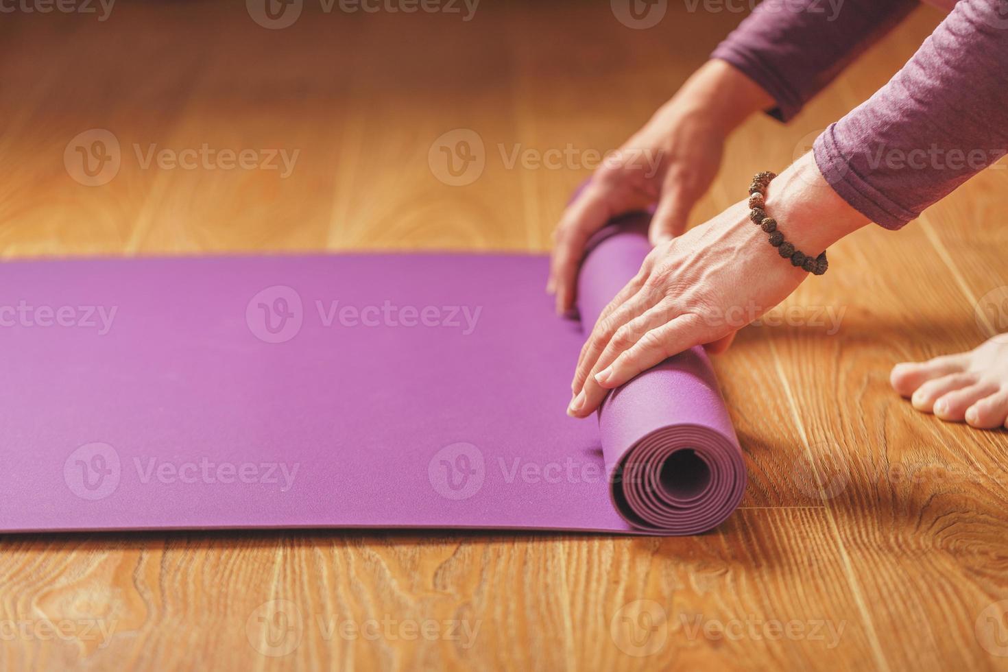 een Mens legt uit een lila yoga mat Aan de houten verdieping van een huis foto