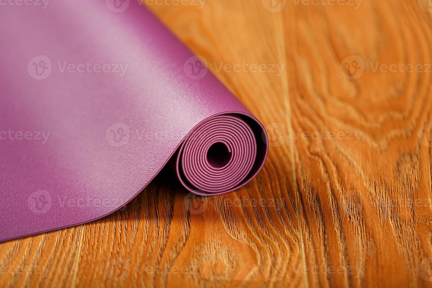 een lila yoga mat is gedraaid Aan de houten vloer. foto