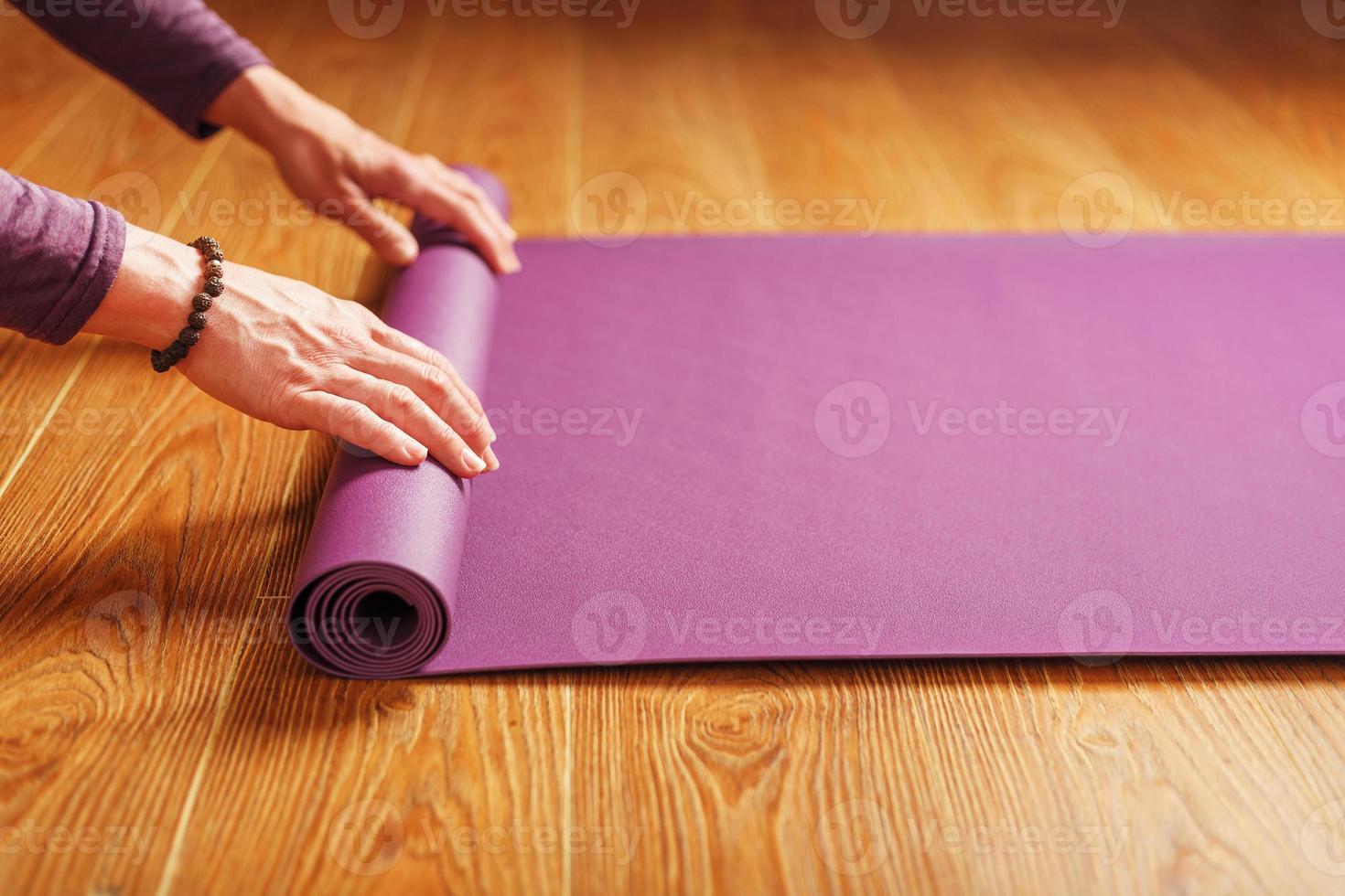 een meisje legt uit een lila yoga mat voordat een training praktijk Bij huis Aan een houten vloer. foto