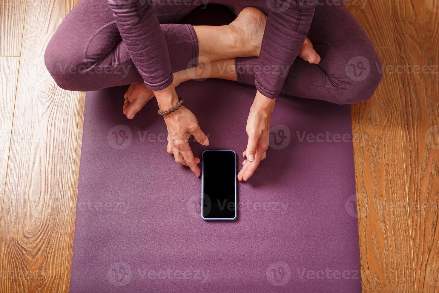 een meisje beoefenen yoga en meditatie Bij huis Aan een lila tapijt gebruik makend van een smartphone en een mobiel app. foto