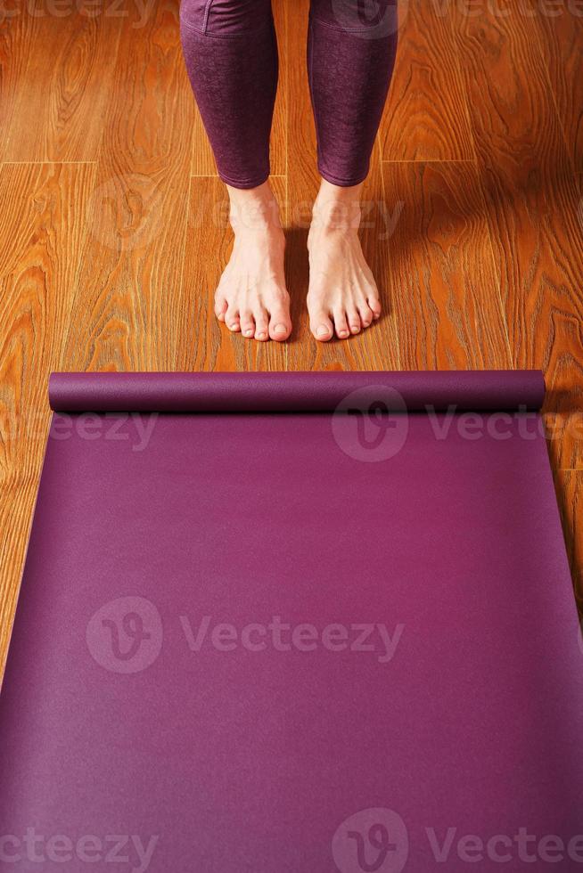 de meisjes voeten staan in voorkant van een ontvouwde yoga mat Aan de houten vloer. foto