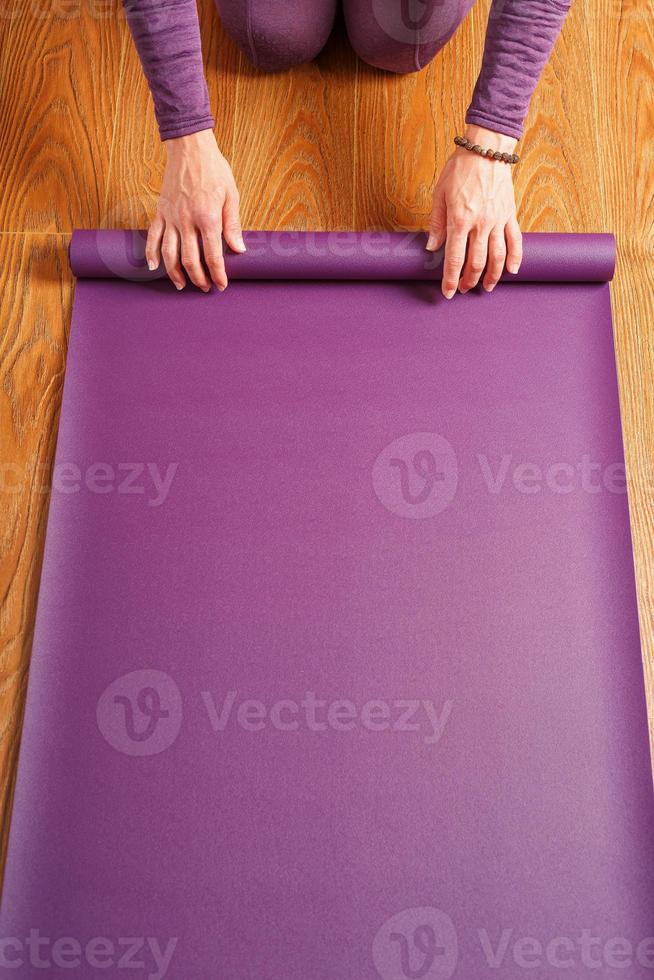 een vrouw legt uit een lila yoga mat Aan de houten vloer. foto