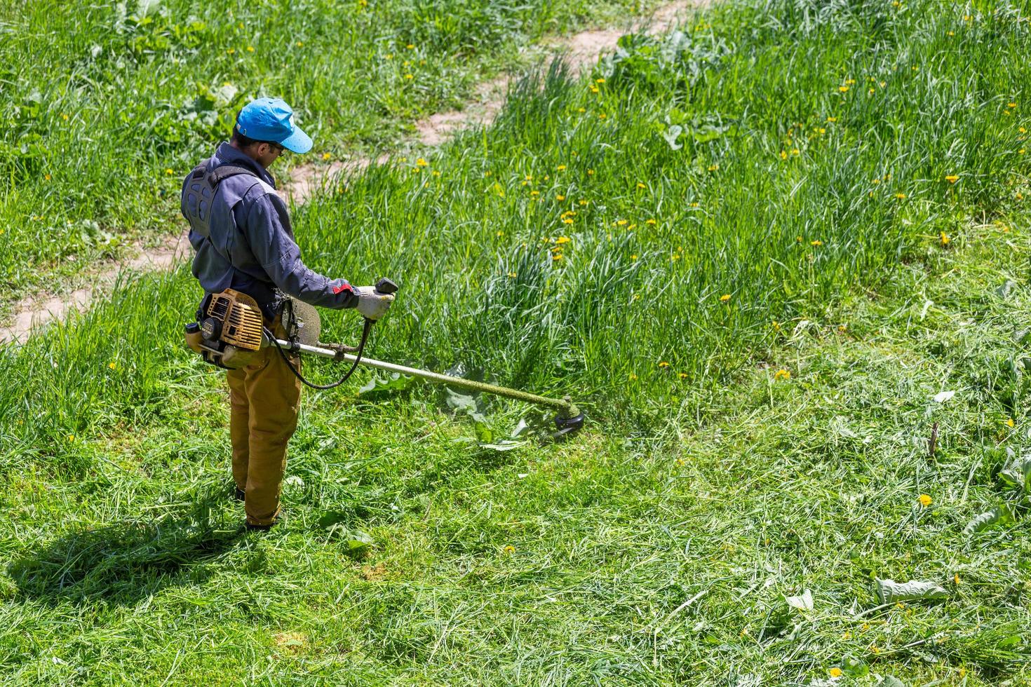 tula, Rusland mei 19, 2020 Russisch officieel grasmaaier arbeider Mens snijdend groen gras met twee-cyclus motor draad trimmer. top naar naar beneden visie. foto