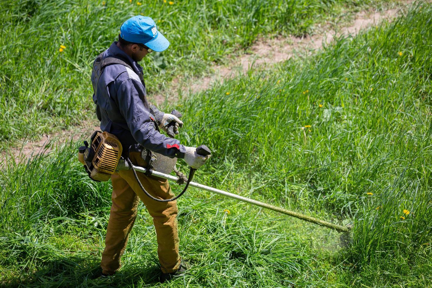tula, Rusland mei 19, 2020 Russisch officieel grasmaaier arbeider Mens snijdend groen gras met twee-cyclus motor draad trimmer. top naar naar beneden visie. foto