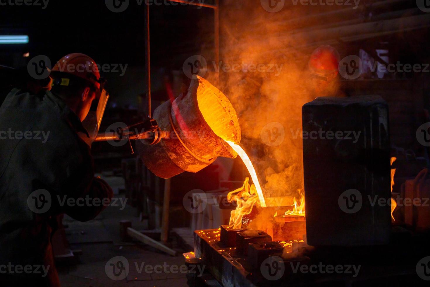 twee arbeiders vulling uit gietvorm met gesmolten metaal in fabriek. foto