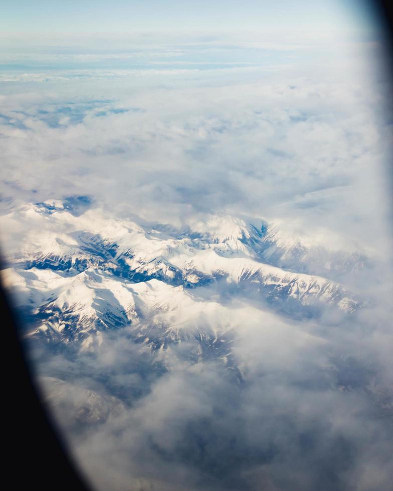 bergketens bedekt met wolken vanuit het raam van een vliegtuig foto