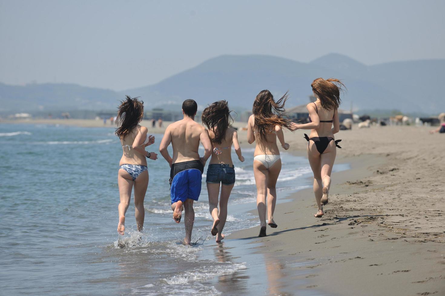 gelukkig mensen groep hebben pret en rennen Aan strand foto