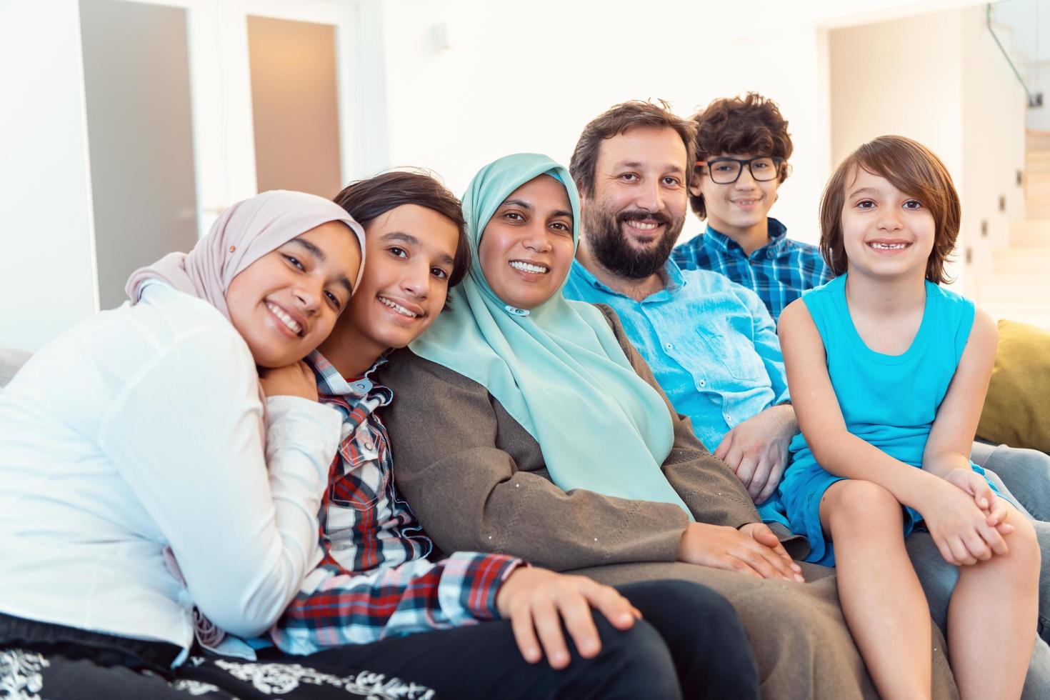 portret foto van een Arabisch moslim familie zittend Aan een bankstel in de leven kamer van een groot modern huis. selectief focus