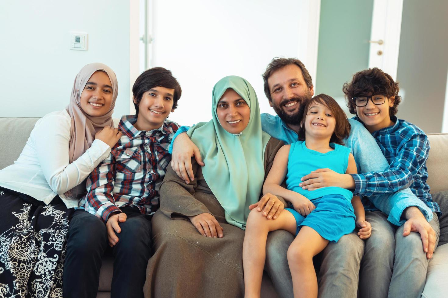 portret foto van een Arabisch moslim familie zittend Aan een bankstel in de leven kamer van een groot modern huis. selectief focus