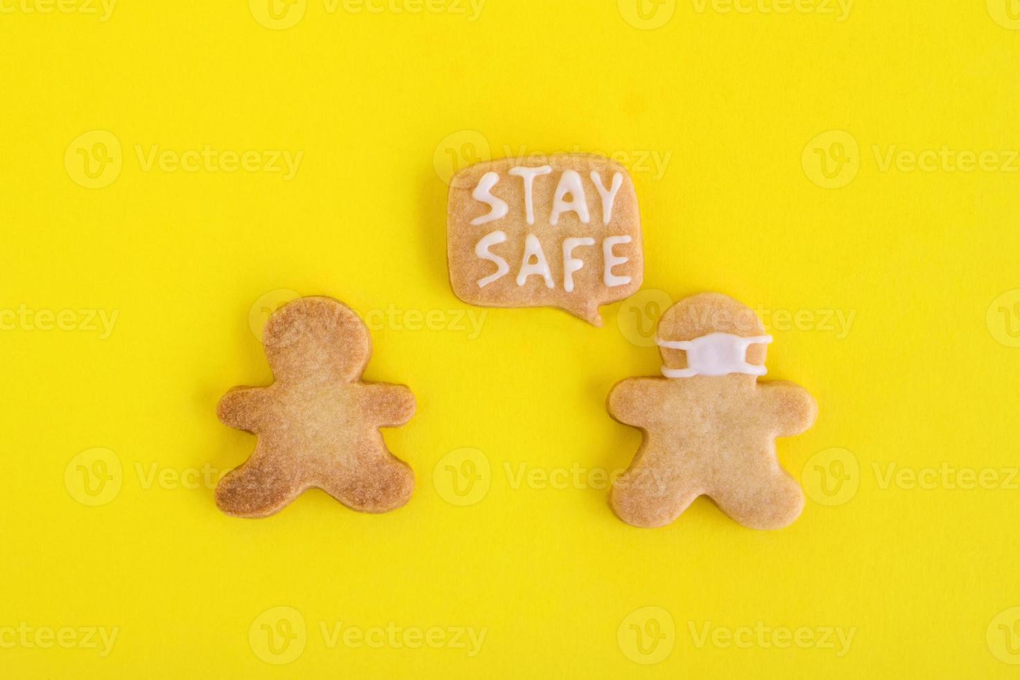 eigengemaakt zandkoekjes koekjes met wit glazuur Aan geel achtergrond, top visie. twee mannen een van hen in gezicht masker en met uitroepen wolk met tekst - blijven veilig foto