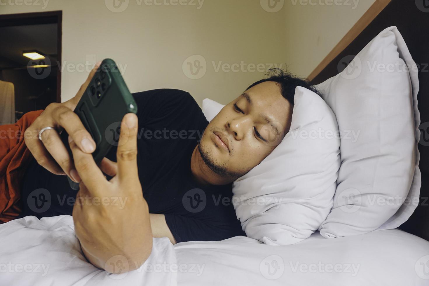 moe jong Mens controle Aan zijn telefoon terwijl aan het liegen in bed foto