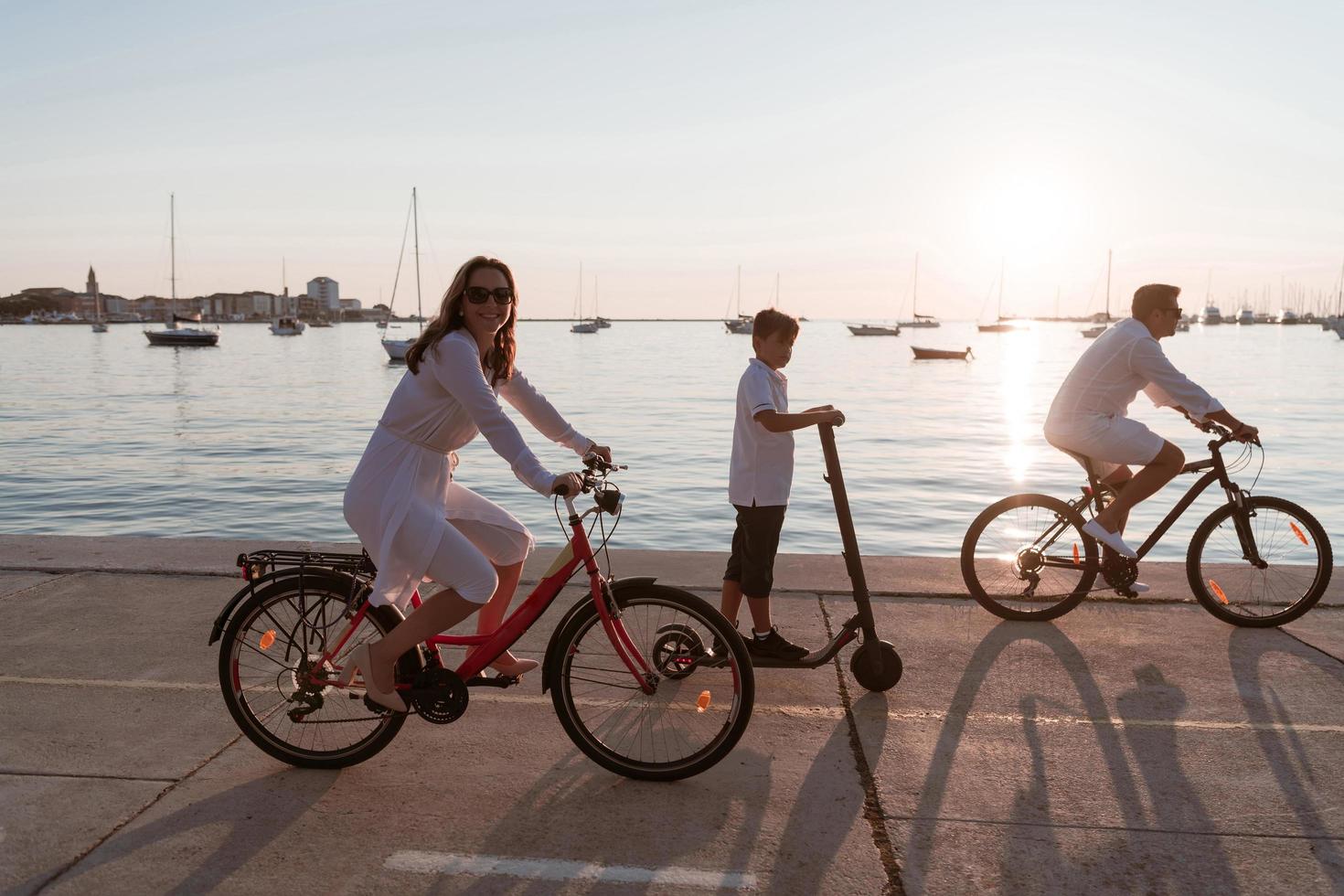 gelukkig familie genieten van een mooi ochtend- door de zee samen, ouders rijden een fiets en hun zoon rijden een elektrisch scooter. selectief focus foto