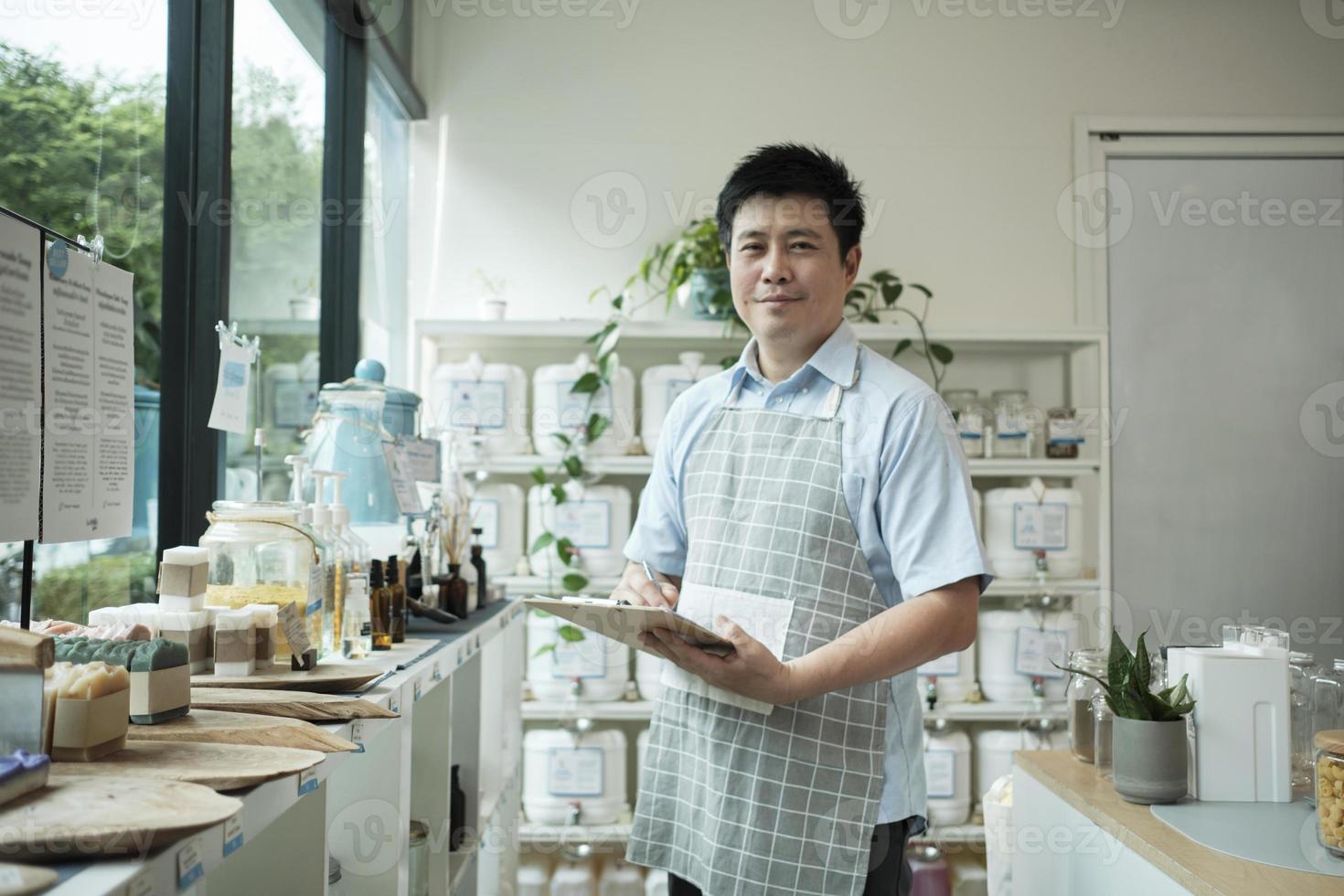 portret van een Aziatisch mannetje winkelier glimlachen en op zoek Bij camera, regelt natuurlijk producten Bij bijvullen op te slaan, Zero waste boodschap, en plasticvrij, eco milieuvriendelijk, duurzame levensstijlen. foto