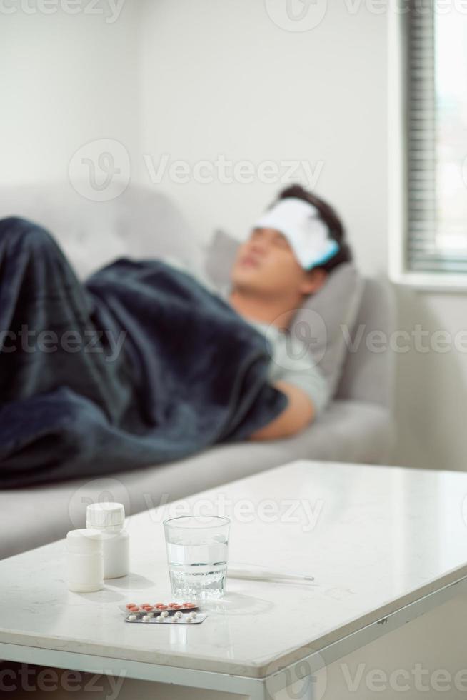 ziek verspild Mens aan het liegen in sofa lijden verkoudheid en winter griep virus hebben geneeskunde tablets in Gezondheid zorg concept op zoek temperatuur Aan thermometer foto