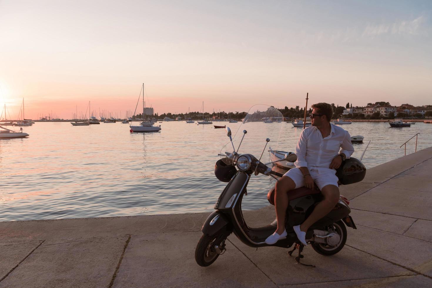 een modern senior zakenman in gewoontjes kleren zittend Aan een scooter door de zee en geniet de zonsopkomst. selectief focus foto