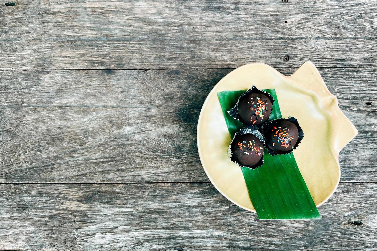 choc ballen of chocola ballen topping met veelkleurig regenboog hagelslag en gekleurde suiker bloem in geel keramisch schotel Aan houten tafel. foto