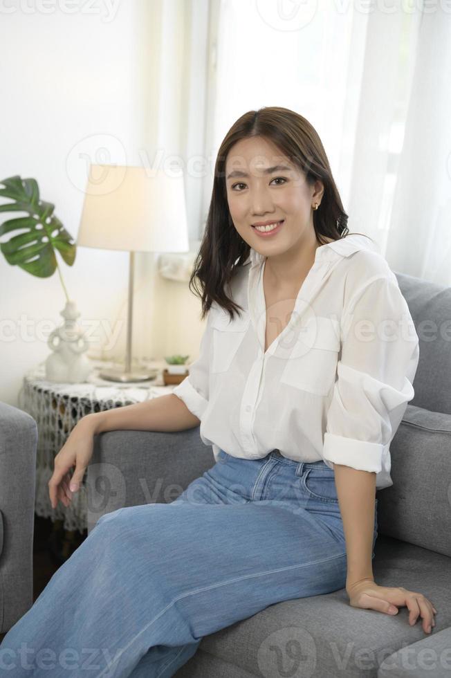portret van jong Aziatisch vrouw glimlachen Aan sofa in leven kamer foto