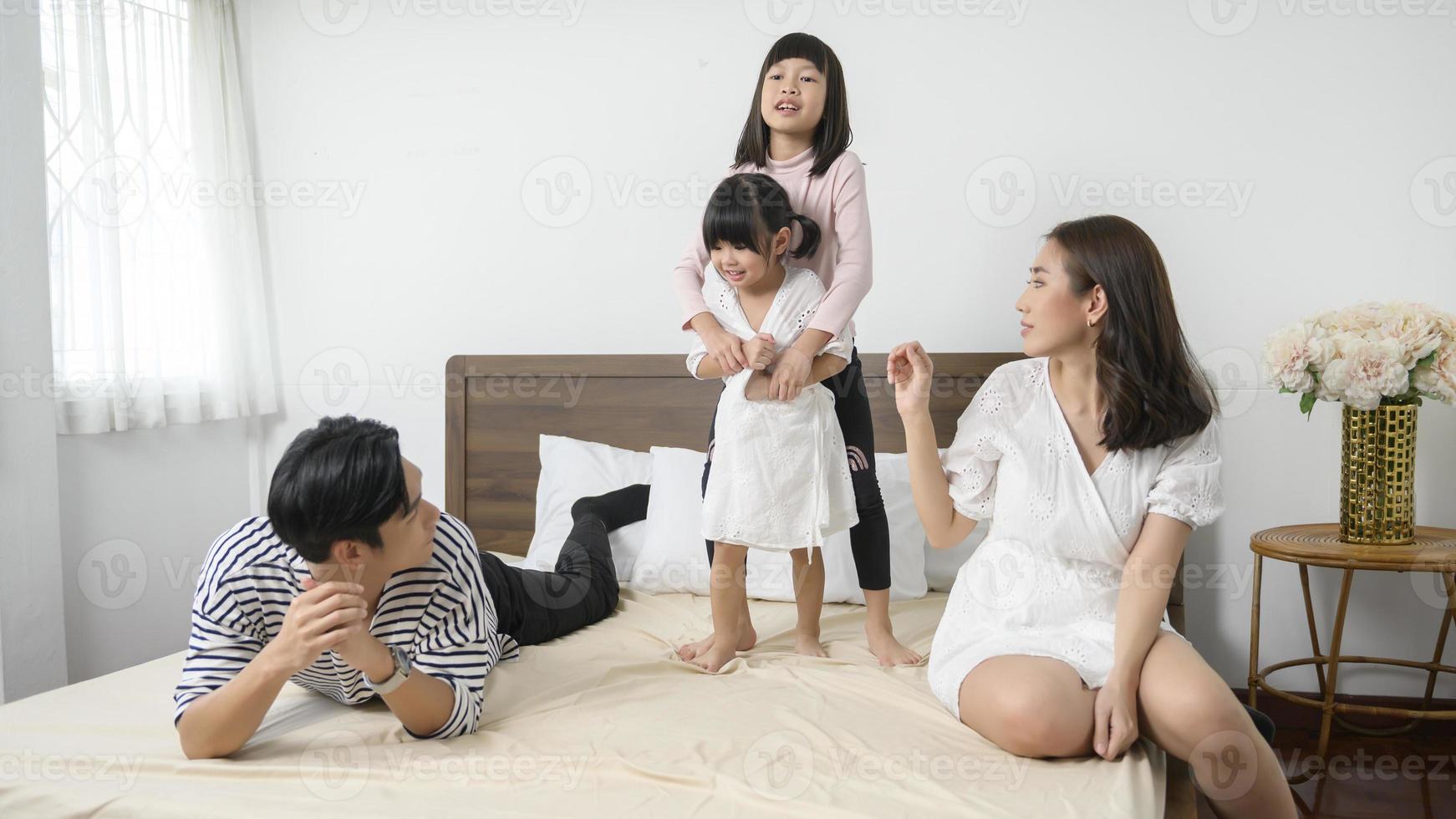 Aziatisch ouders met twee weinig dochters jumping Aan de bed in slaapkamer, gelukkig familie concept foto