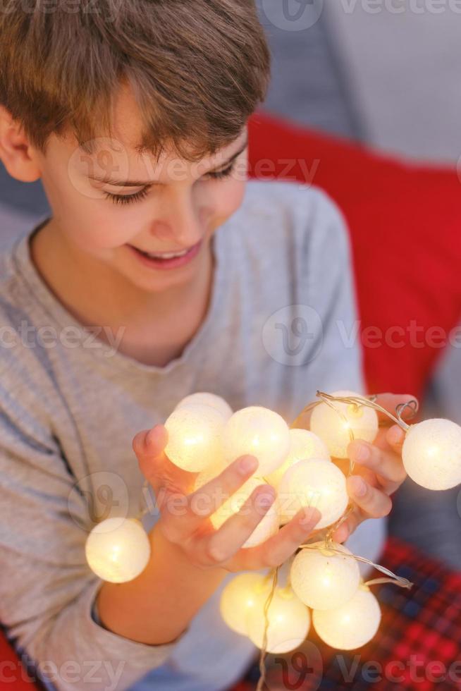 detailopname van tiener- jongen met verlichte Kerstmis lichten Bij huis foto