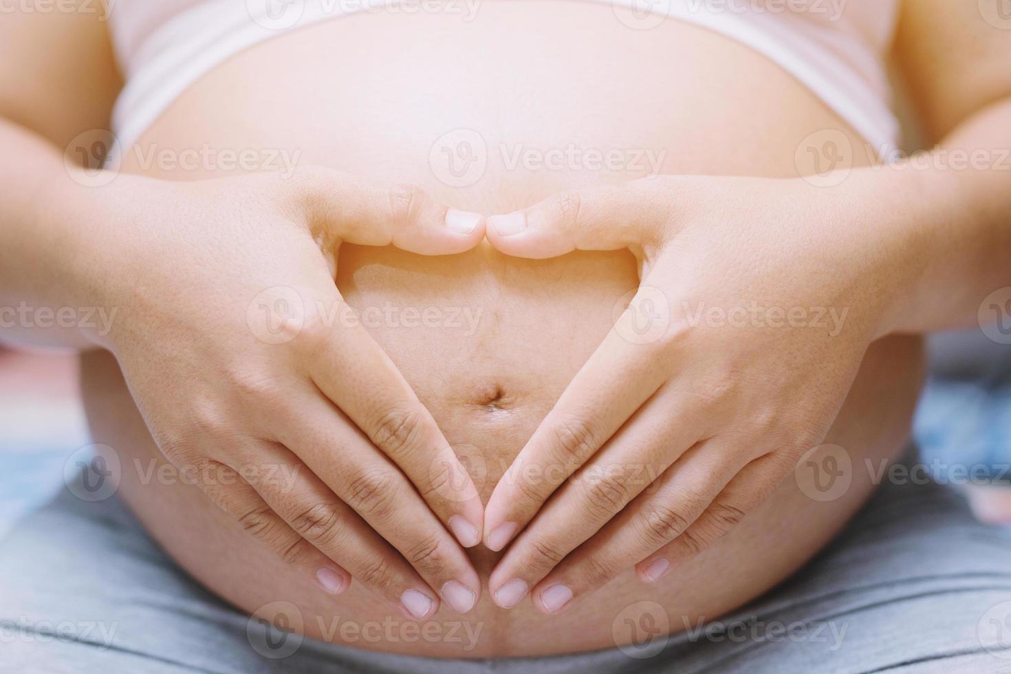 nieuw mam zwanger vrouw in wit ondergoed hartvormig hand- tonen liefde met baby. jong vrouw ervan uitgaand een baby staan in de buitenshuis. foto