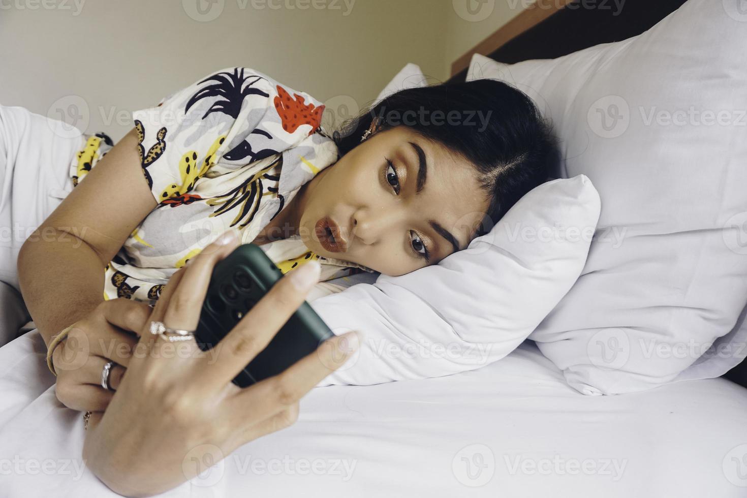 geschokt jong vrouw controle Aan haar telefoon terwijl aan het liegen in bed foto