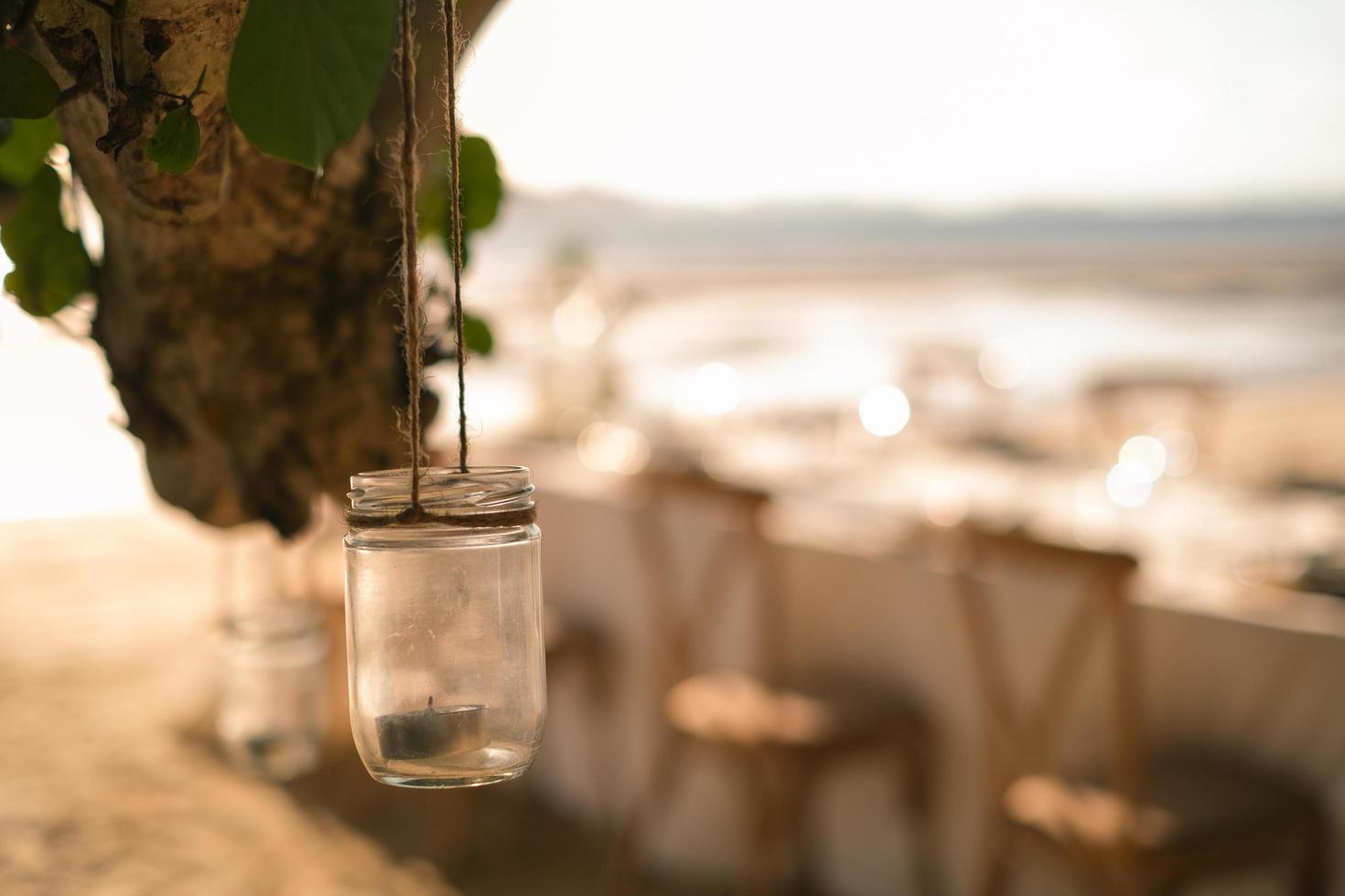 dichtbij omhoog de pot kaars hangende Aan de boom met lang tafel bruiloft avondeten opstelling Aan de strand Bij Thailand in de avond. bruiloft partij concept. decoratie buitenshuis restaurant Bij de strand. foto