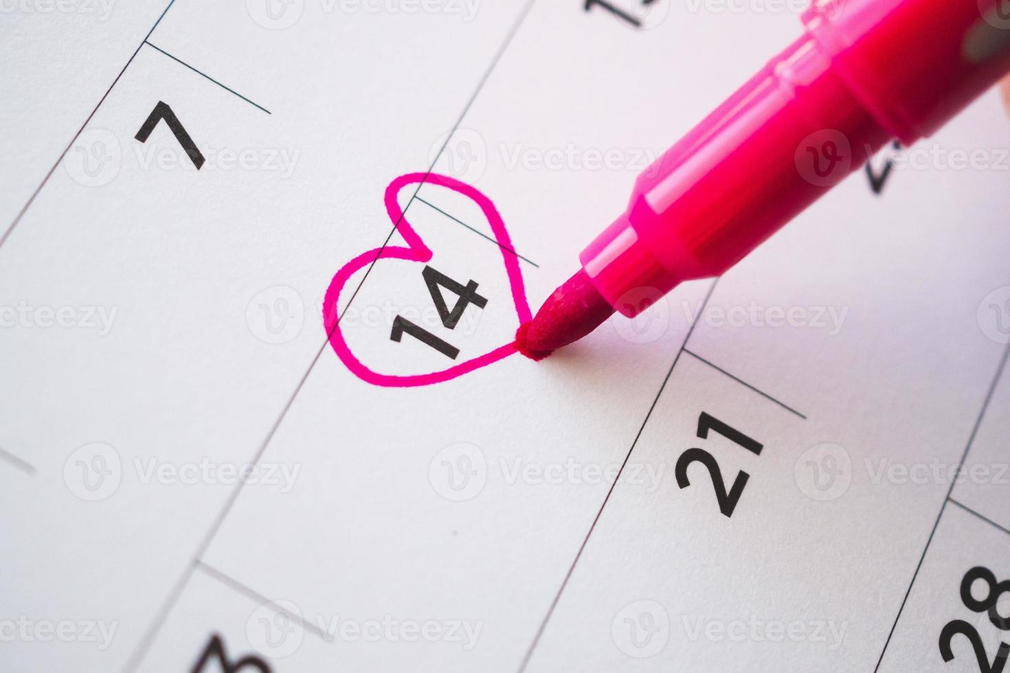 vrouw hand- met pen Mark hart vorm Aan kalender datum Bij 14e Valentijn dag foto