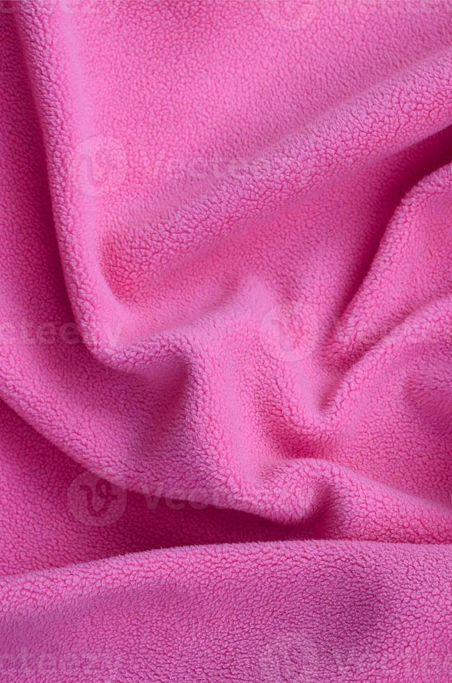 de deken van harig roze fleece kleding stof. een achtergrond van licht roze zacht pluche fleece materiaal met een veel van Verlichting vouwen foto