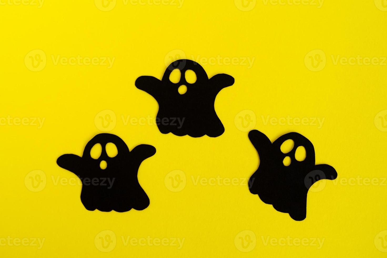 vakantie decoraties voor halloween. drie zwart papier geesten Aan een geel achtergrond, top visie. foto