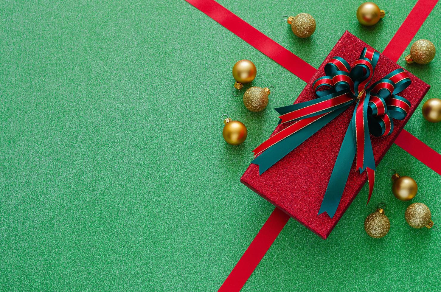 rood geschenk doos met boog lint en Kerstmis kerstballen ornamenten Aan groen achtergrond. Kerstmis en nieuw jaar concept. foto
