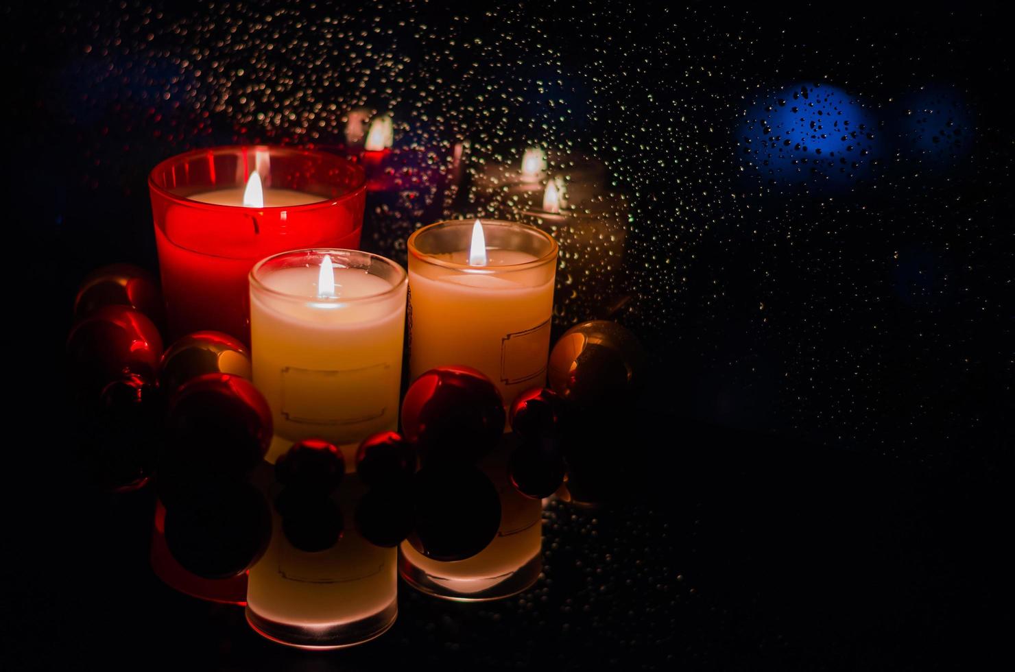 focus en wazig van brandend kaarsen met chirstmas ornamenten zetten naast venster dat hebben regen laten vallen in donker achtergrond. foto