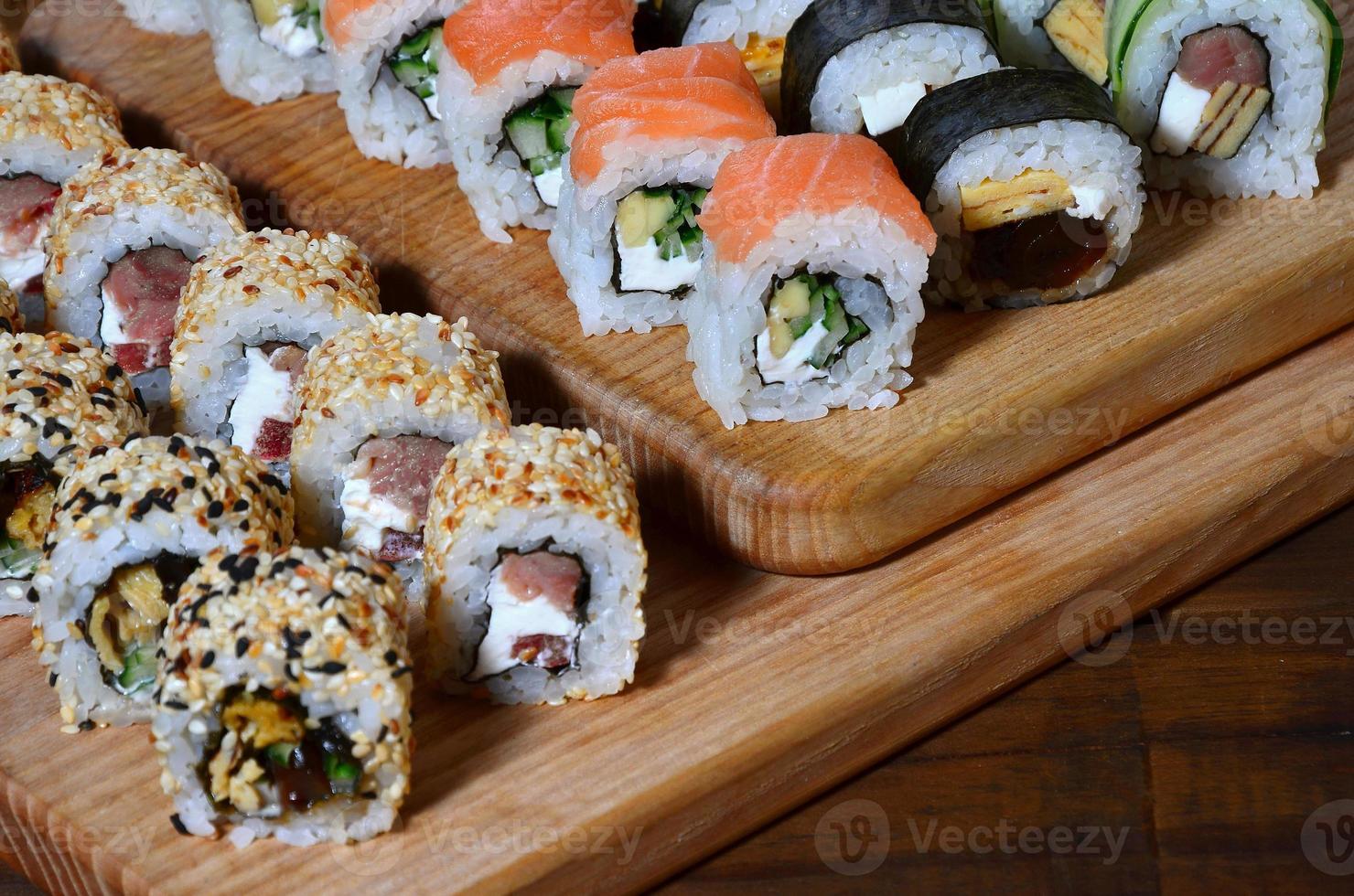 sushi reeks van een aantal van broodjes is gelegen Aan een houten snijdend bord Aan een tafel in de keuken van een sushi bar. een traditioneel schotel van oosters keuken foto