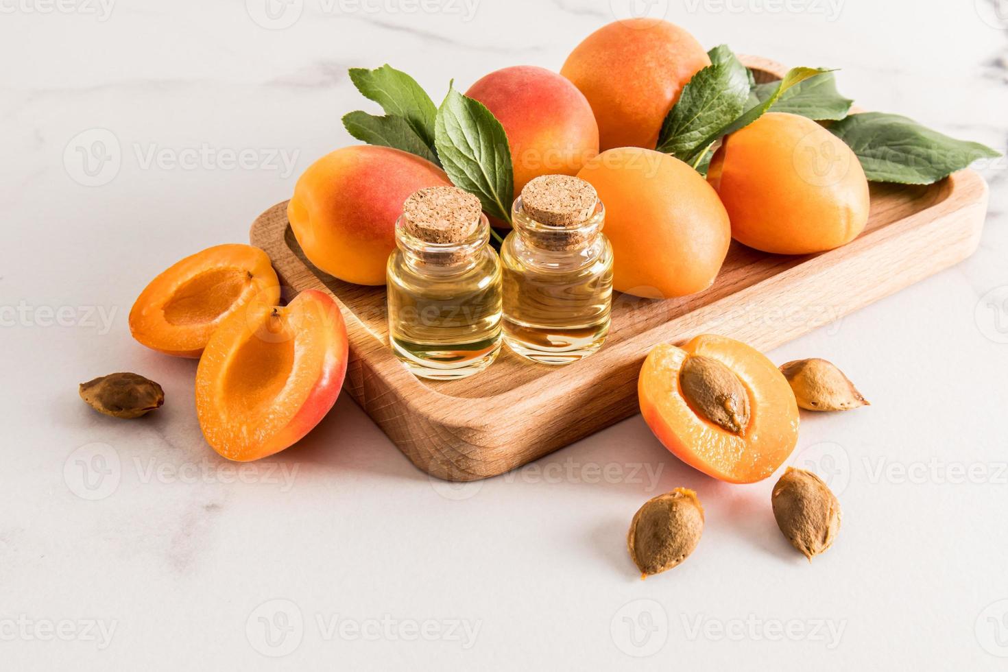 twee glas flessen met een kurk pet met biologisch abrikoos kernel olie staan Aan een houten dienblad van sappig abrikozen. een onthullend natuurlijk zorg. foto