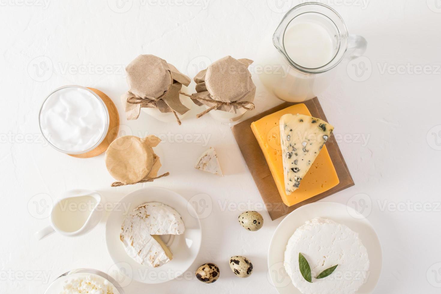 top visie van de wit achtergrond met divers zuivel producten - melk in flessen, verzuren room, huisje kaas in de schaal, kaas Aan een houten bord. foto