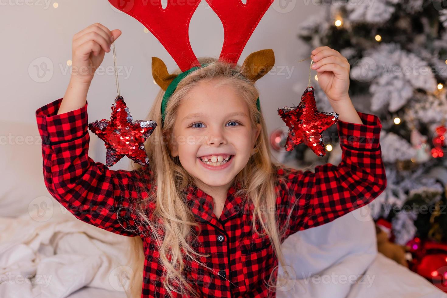 gelukkig weinig blond meisje Bij huis in pyjama voor Kerstmis sorteren presenteert en spelen met Kerstmis speelgoed foto