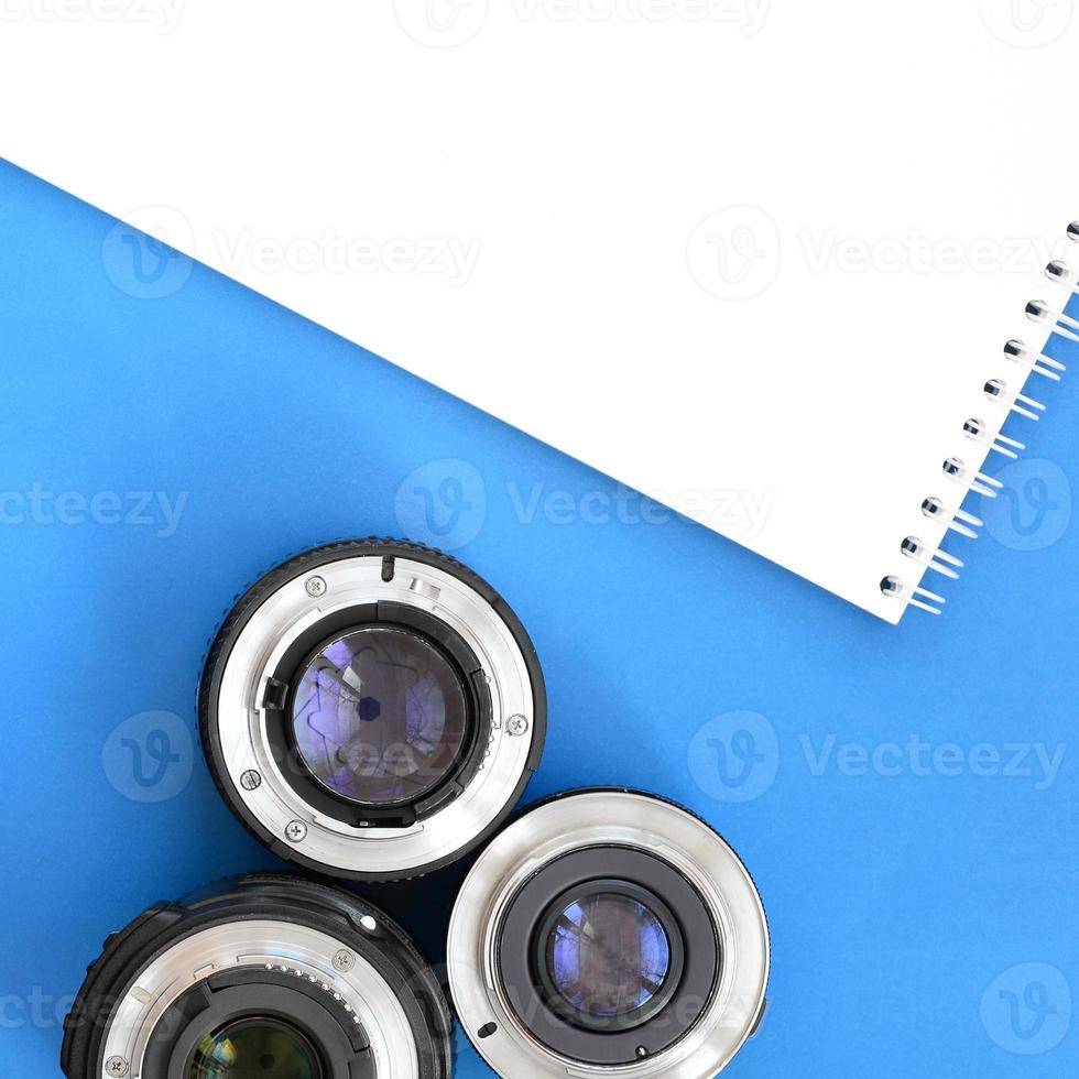 meerdere fotografisch lenzen en wit notitieboekje liggen Aan een helder blauw achtergrond. ruimte voor tekst foto