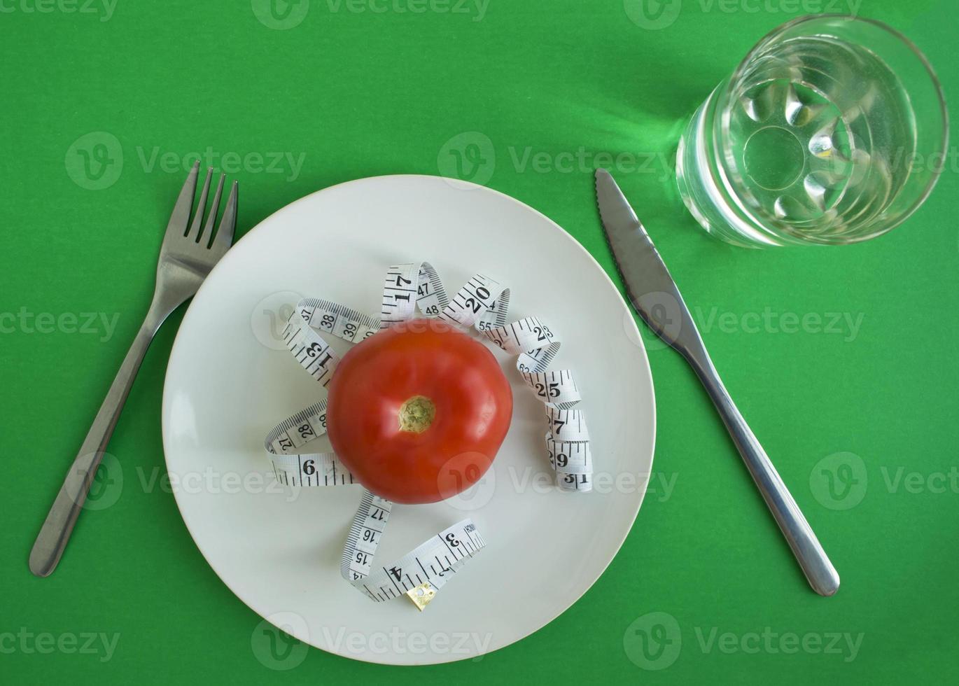 tomaat en centimeter plakband in een bord, vork en mes, een glas van water foto