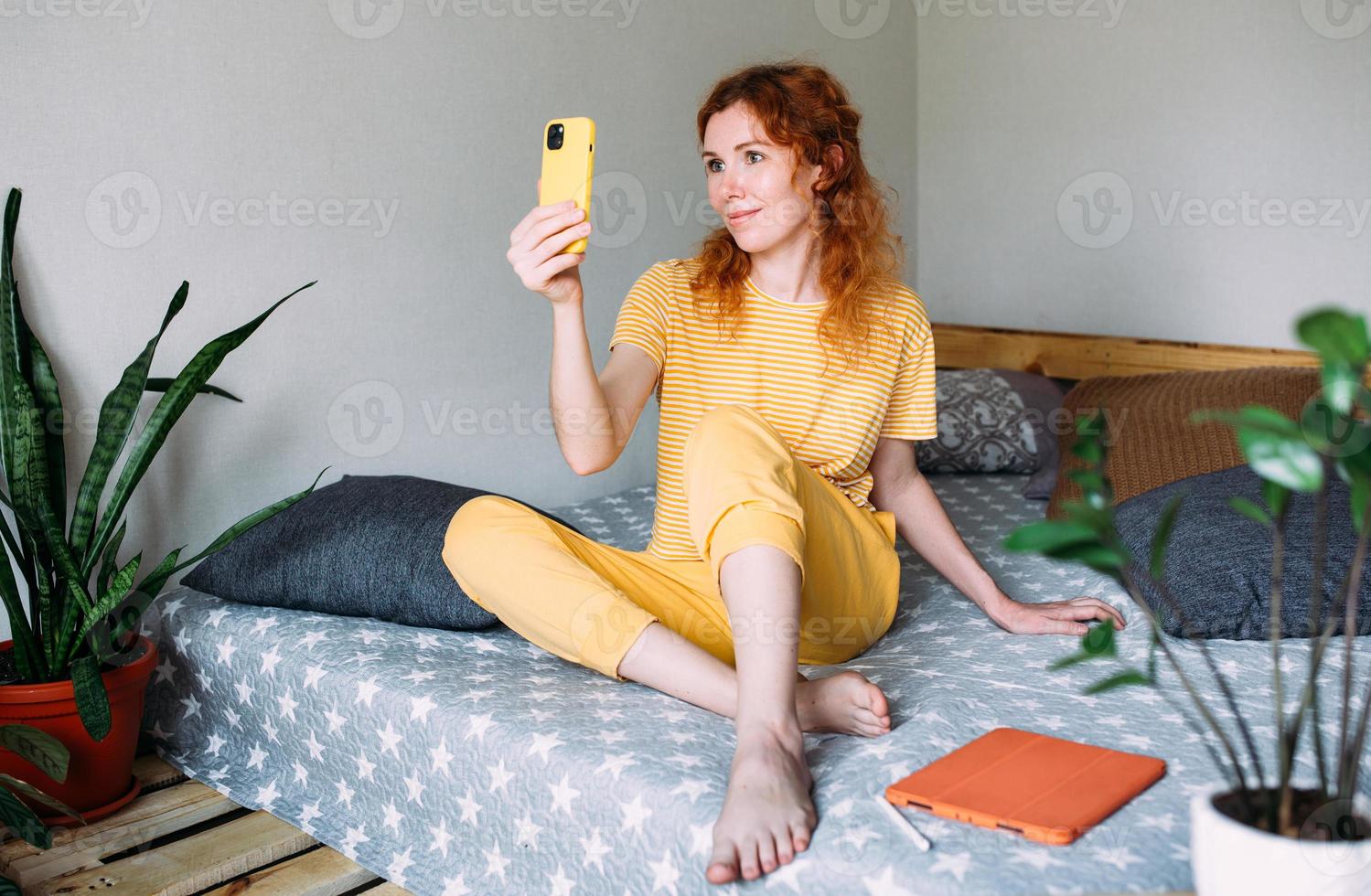 jong roodharig meisje maakt een selfie thuis op de bank op een smartphone foto